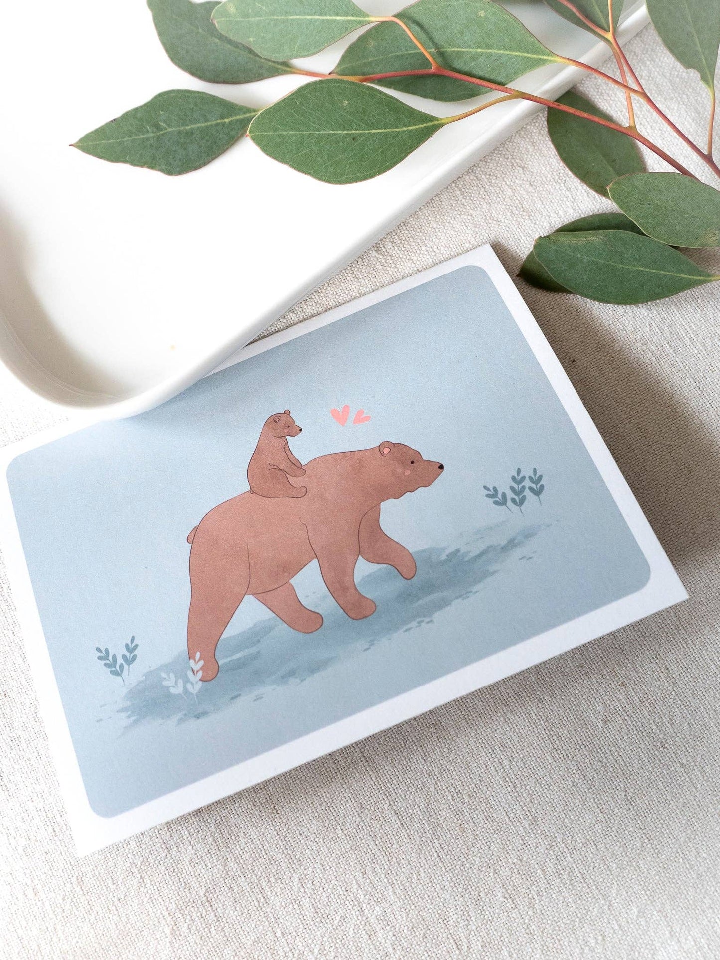 Postikortti "Karhun sylillinen rakkautta" – Saima Visuals, avattava A6-kokoinen kortti kierrätyskartongista, mukana valkoinen kirjekuori.