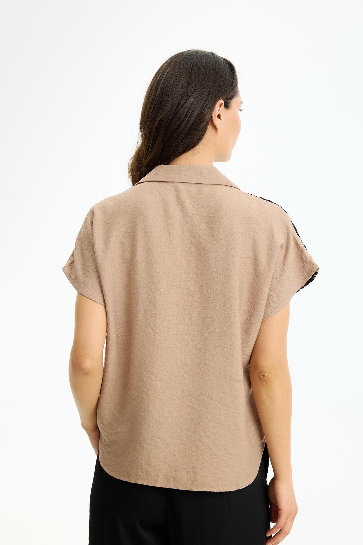 Hiekanvärinen kevyesti laskeutuva naisten pusero, jossa mustat pitsikoristeet olkapäillä ja yläosassa sekä V‑pääntie kauluksella.